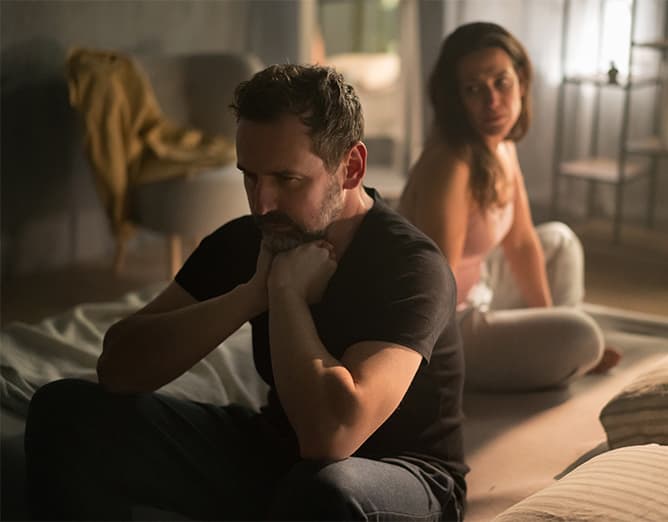 A couple sitting apart in a dim room